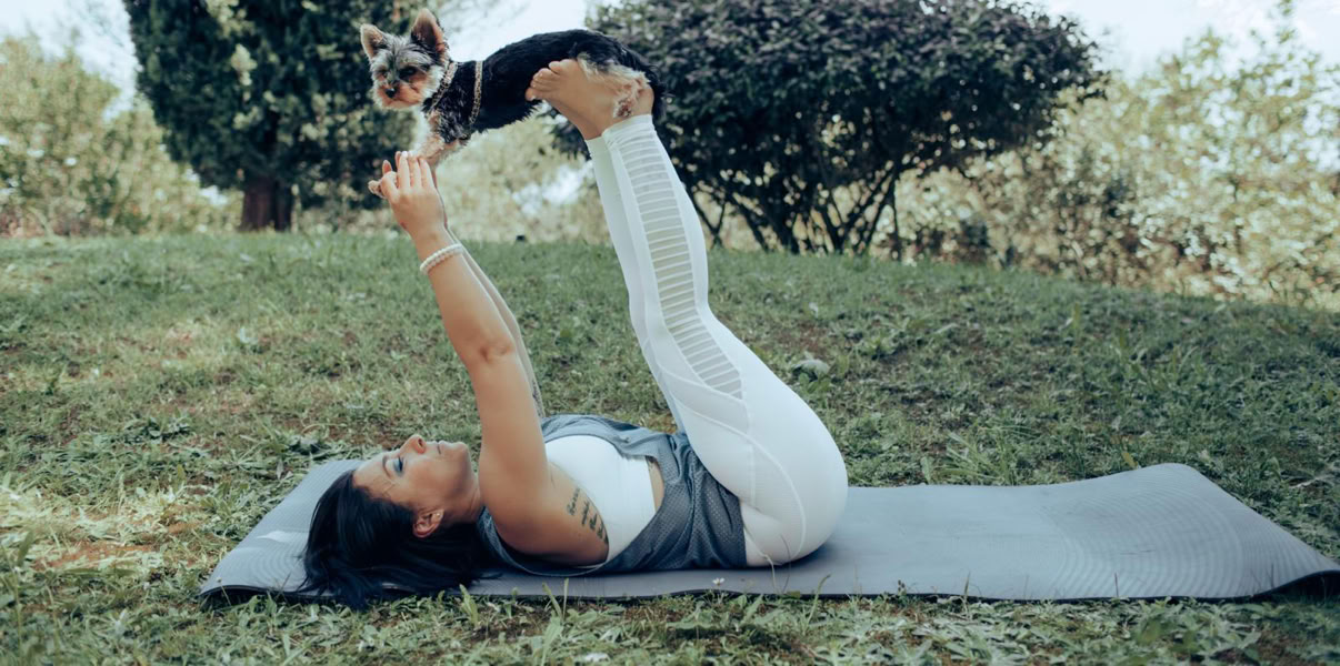 Une pratiquante allongée sur le dos lève les jambes pendant une séance de Doga en extérieur.