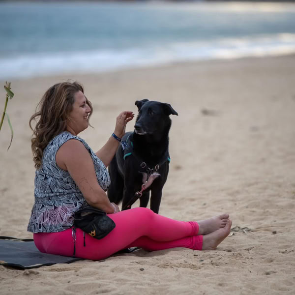 Femme assise sur la plage partageant un moment de complicité avec son chien noir.