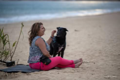 Une pratiquante assise sur son tapis à la plage, accompagnée de son chien.
