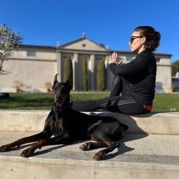 Femme assise en posture de yoga à côté de son dobermann en extérieur.