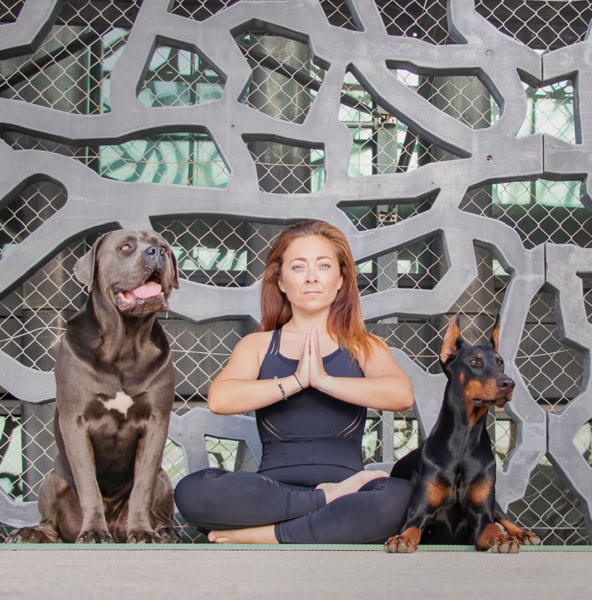 Une pratiquante assise en tailleur sur son tapis, entourée de chiens.